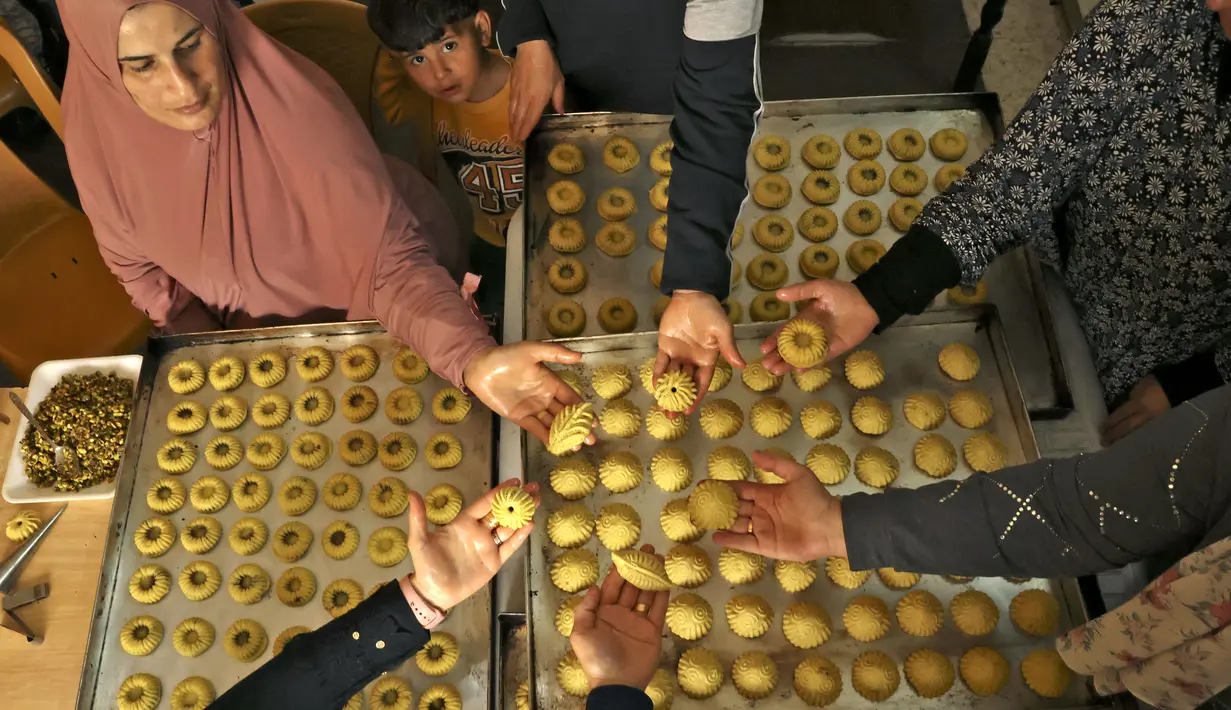 <p>Perempuan Palestina membuat kue tradisional berisi kurma dan kacang-kacangan dalam persiapan untuk liburan Idul Fitri, di kota Hebron, Tepi Barat, pada 28 April 2022. Orang-orang di Palestina mempunyai tradisi lebaran yang unik dan khas yaitu dengan membuat kue kering dengan aneka bentuk dan rasa. (HAZEM BADER / AFP)</p>