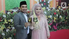 Sepasang pengantin menunjukkan buku nikah seusai prosesi ijab-kabul di KUA Pamulang, Tangerang Selatan, Selasa (22/2/2022). Sebanyak 10 pasangan menjalankan akad nikah di KUA Pamulang pada hari ini yang dianggap memiliki tanggal cantik. (merdeka.com/Arie Basuki)