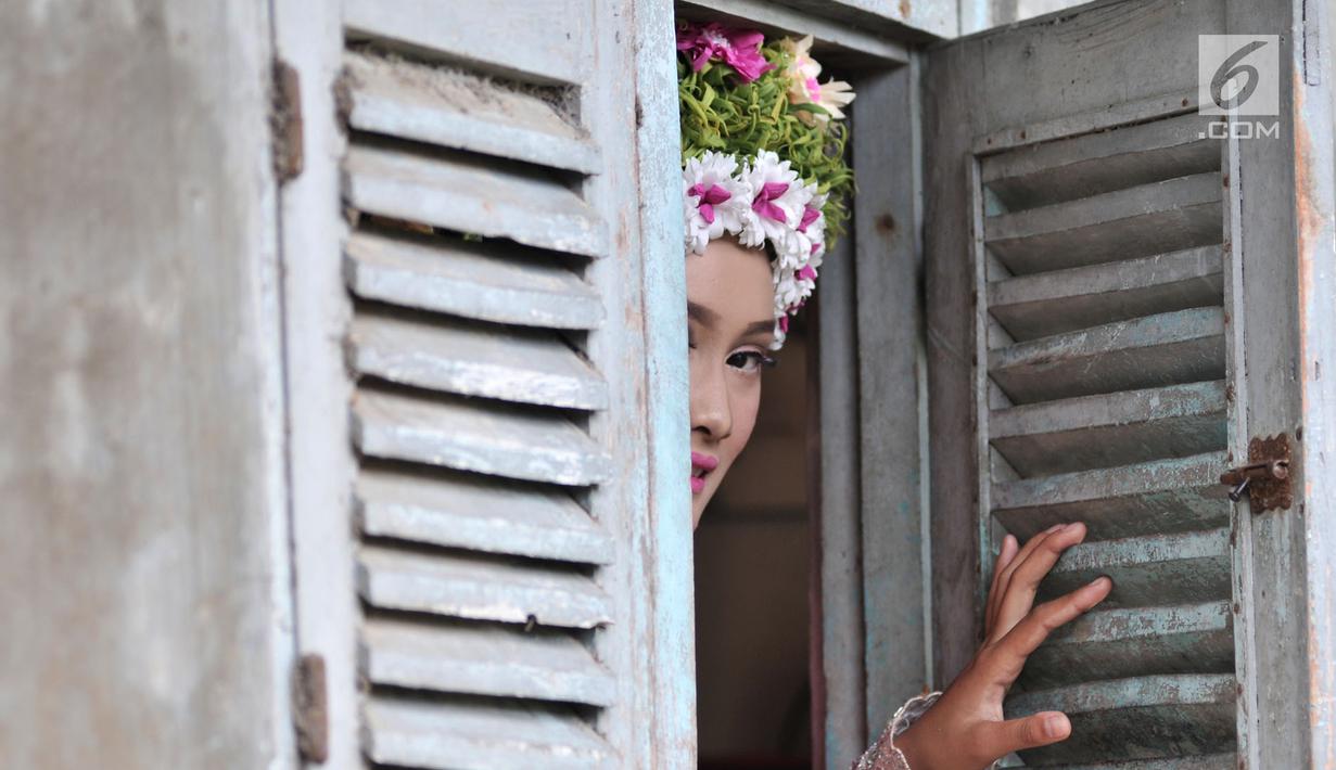 Seorang gadis mengintip dari jendela rumah saat hendak mengikuti upacara adat Ngarot di Desa Lelea, Indramayu, Jawa Barat, Rabu (19/12). Para gadis dihias dengan berbagai jenis bunga warna-warni yang dianggap simbol kesuburan. (Merdeka.com/Iqbal Nugroho)