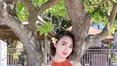 Wika Salim saat berpose di bawah pohon mengenakan dress mini warna oranye model halter. Ia menyelipkan bunga di telinganya agar mempermanis penampilannya. (Instagram/wikasalim)