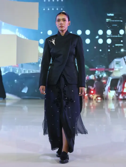 Adinia Wirasti tampil dengan kebaya janggan warna hitam dhiasi bros besar. Dipadukan bawahan kain hitam dengan asken tille dan bordiran keemasan serta sandal slop warna senada. [Adrian/Fimela]