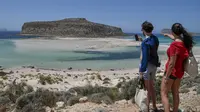 Sepasang wisatawan melihat Pantai Balos dan laguna di barat laut Pulau Kreta, Yunani, Kamis (13/5/2021). Yunani mempermudah langkah-langkah terkait COVID-19 dalam menyambut turis internasional pada 14 Mei. (Louisa GOULIAMAKI/AFP)