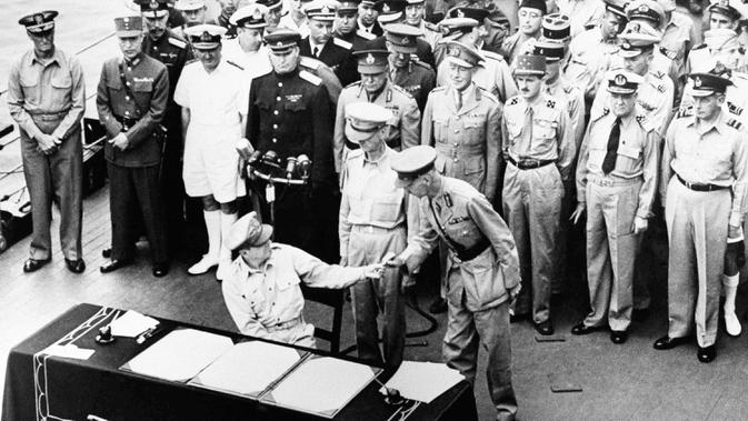 Jenderal AS Douglas MacArthur menyerahkan pena kepada Letnan Inggris Jenderal Arthur E. Percival usai menandatangani surat-surat penyerahan Jepang di atas kapal perang USS Missouri, Teluk Tokyo, 2 September 1945. Penandatanganan ini menandai berakhirnya Perang Dunia II. (Pool Photo via AP, File)