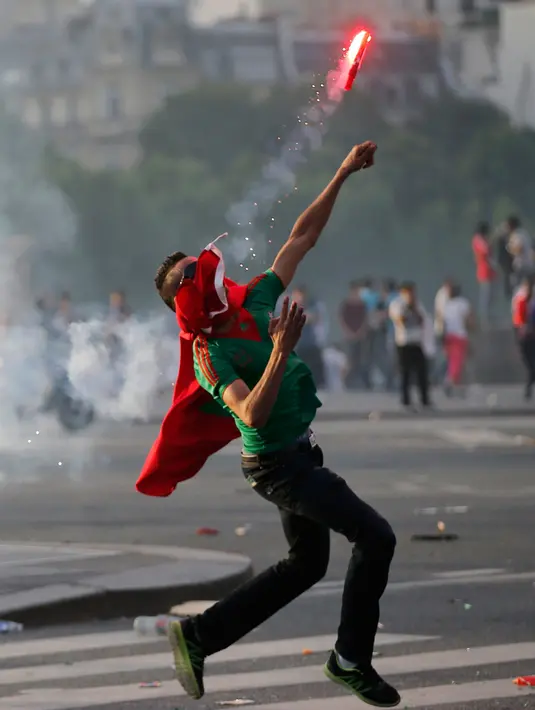 Demonstran melemparkan kembali gas air mata yang baru ditembakkan petugas kerusuhan di bawah Menara Eiffel di dekat zona penggemar Paris sebelum laga Portugal vs Prancis di Final EURO 2016 di Prancis (10/6). (REUTERS/Stephane Mahe)