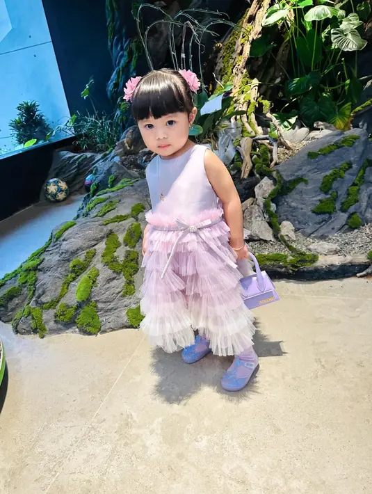 Kali ini, kakak Azura ini tampil manis kenakan ruffle tulle dress warna lilac dengan tas Jacquemus leather top-handle bag yang harganya capai jutaan rupiah. [@aurelie.hermansyah/@sus.irohh].