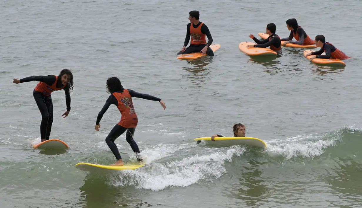 Pelajar selancar menaiki papan mereka di Pantai Carcavelos, di luar Lisbon, Selasa (12/7/2022). Portugal mengalami gelombang panas yang membuat pemerintah mengumumkan keadaan siaga mulai Senin hingga Jumat karena meningkatnya risiko kebakaran hutan. (AP Photo/Armando Franca)