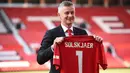 Ole Gunnar Solskjaer menunjukkan jersey Manchester United saat konferensi pers di Stadion Old Trafford, Inggris, (28/3). MU mengontrak Solskjaer selama tiga tahun. (AFP Photo/Oli Scarff)