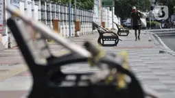 Pemulung melintasi deretan bangku trotoar yang disegel garis pembatas dan ditutupi bambu, Rawamangun, Jakarta, Minggu (3/5/2020). Bangku trotoar di sepanjang jalan Rawamangun disegel untuk mencegah kerumunan warga sebagai upaya memutus rantai penyebaran COVID-19. (merdeka.com/Iqbal S. Nugroho)