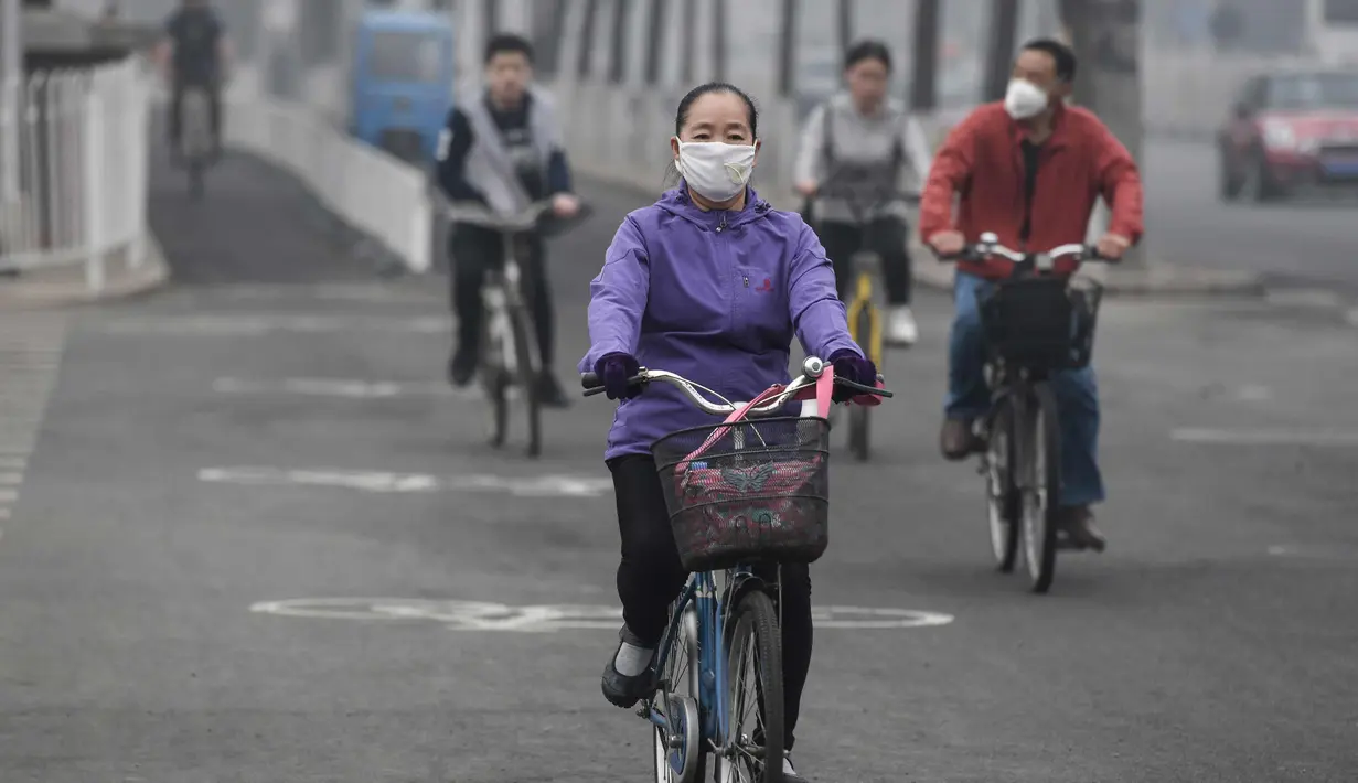 Warga mengendarai sepeda dengan memakai masker pada hari yang tercemar polusi udara di Beijing, China (2/4). (AFP Photo/Fred Dufour)