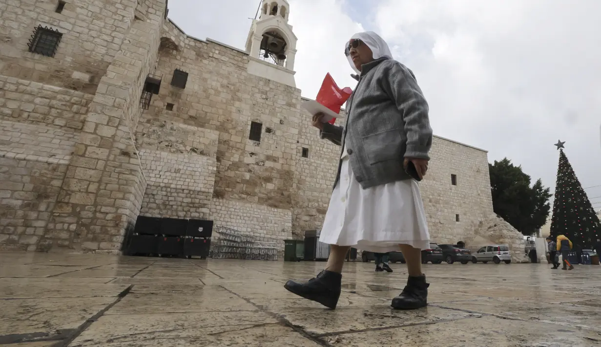 Seorang biarawati Kristen berjalan menjelang Natal di luar Gereja Kelahiran Yesus di kota Bethlehem, Tepi Barat pada 22 Desember 2022. Beberapa tempat indah yang diincar pengunjung menyambut Natal di Kota Bethlehem adalah Gereja Kelahiran yang sudah berusia ratusan tahun. (AFP/Hazem Bader)