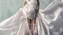 Gaun putih tersebut memiliki model rok pendek di bagian depan dan flowy panjang di bagian belakang. Melengkapinya dengan kaos kaki putih sheer cut out depan berpita dan renda. [@valerieethomas]