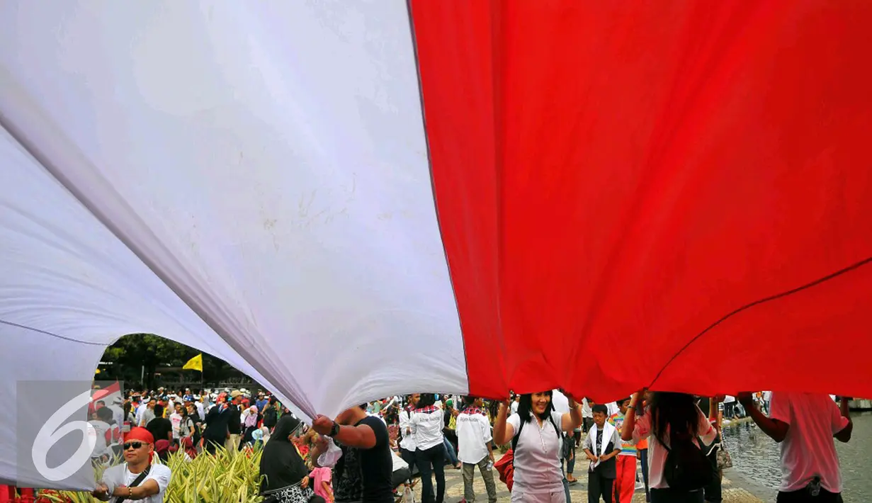 Seorang peserta 'Aksi Kita Indonesia' membentangkan Bendera Merah Putih raksasa di Bundaran HI, Jakarta, Minggu (4/12). Mereka juga membawa berkeliling Bendera Merah Putih raksasa sambil meneriakkan 'Kita Indonesia'. (Liputan6.com/Angga Yuniar)