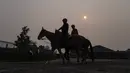 Kabut asap dari kebakaran hutan di bagian utara menutupi sinar matahari pada Rabu pagi saat para penunggang kuda menunggangi tunggangannya menuju lintasan menjelang pacuan kuda Belmont Stakes yang dijadwalkan berlangsung pada hari Sabtu. (AP Photo/John Minchillo)