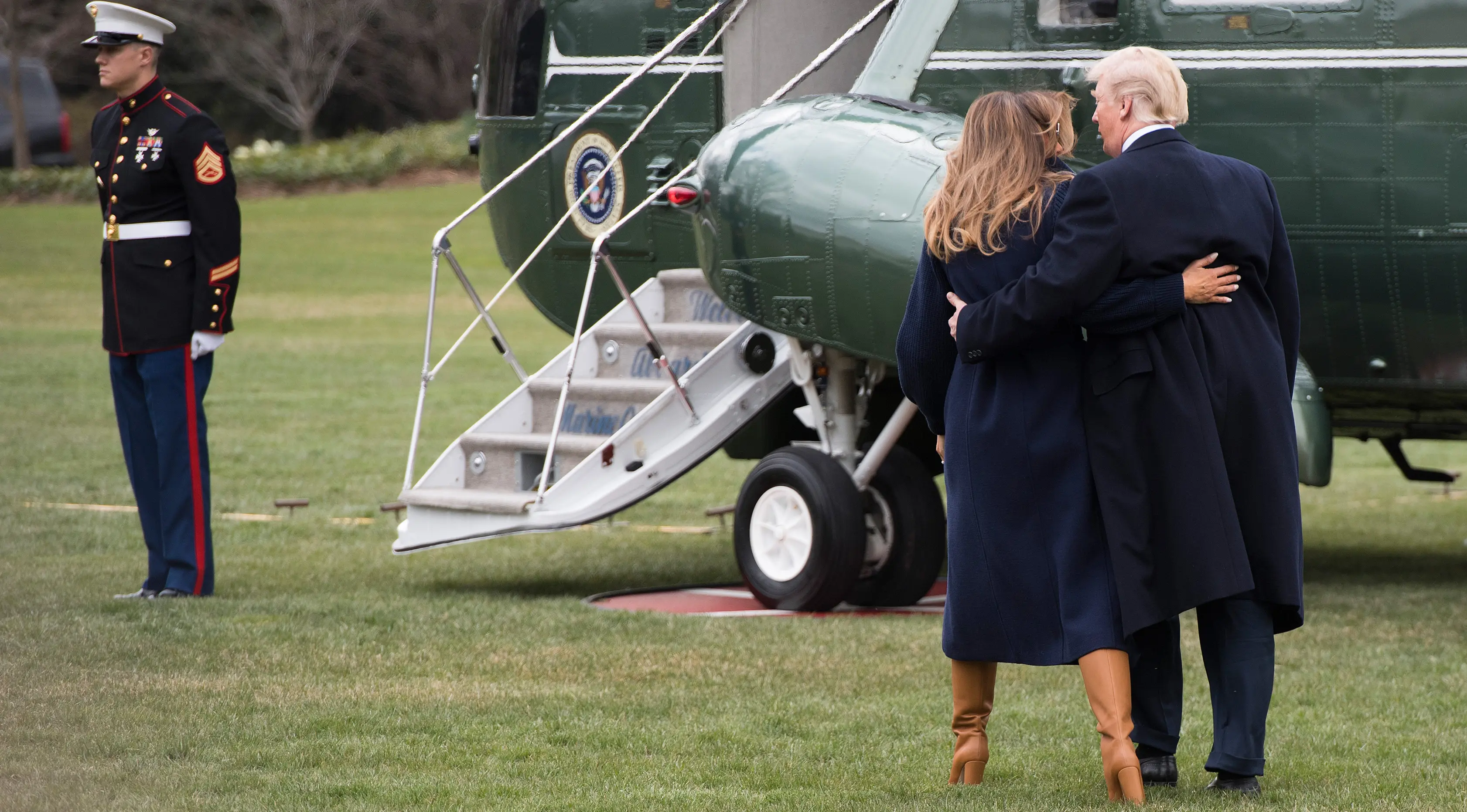 Presiden AS Donald Trump terlihat memegang ibu negara, Melania Trump yang hampir terjatuh saat berjalan menuju helikopter kepresidenan di halaman berumput Gedung Putih, Senin (19/3). Trump dan Melania hendak bertolak ke New Hempshire. (JIM WATSON/AFP)