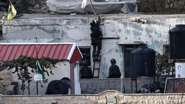 Seorang tentara Israel menyingkirkan bendera dari atap sebuah rumah selama serangan militer di Qabatiya, Tepi Barat. [Zain Jaafar/AFP]