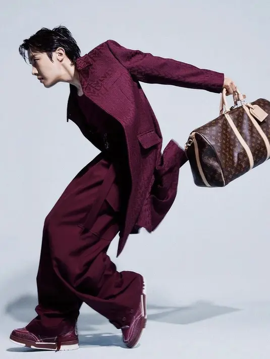 J-Hope juga mengenakan setelan merah maroon dengan atasan jas panjang bertuliskan LV. Ia pun memamerkan tas LV besar warna Coklat bertuliskan LV.  Credit: Louis Vuitton