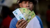 Seorang pria menunjukkan mata uang uang lokal yang baru di Caracas, Venezuela (15/12). Mata uang ini  bisa ditukarkan secara lokal untuk makanan pokok seperti gula, beras dan roti yang diproduksi di lingkungan itu sendiri. (AFP Photo/Federico Parra)