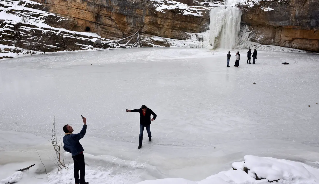 Para pengunjung berada air terjun Mirusha yang membeku di Lapceve, Kosovo (9/1). Cuaca bersuhu mencapai minus 20 derajat celcius membuat Air Terjun Mirusha dan kolam membeku. (AFP Photo/Armend Nimani)