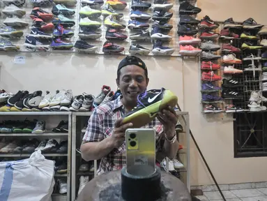 Bajuri (45) saat memasarkan sepatu impor bekas melalui media sosial di toko Second BJR, Kali Baru Timur, Cilincing, Jakarta Utara, Rabu (1/6/2022). Bursa sepatu impor bekas bermerek dalam beberapa tahun terakhir mulai ramai diminati warga lantaran harga yang terjangkau dan kualitas bahan. (merdeka.com/Iqbal S. Nugroho)