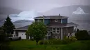 Gunung es terapung terlihat di balik rumah di King's Point, Newfoundland, Kanada, 2 Juli 2019. Potongan besar berwarna putih itu biasa mengapung sepanjang musim semi dan musim panas. (Johannes Eisele/AFP)