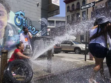 Jennifer Pagan (kiri) menyemprotkan air ke teman-temannya dari hidran kebakaran yang terbuka di bagian The Bronx, New York, Jumat (22/7/2022). Suhu tinggi yang berbahaya mengancam sebagian besar Timur Laut dan Selatan Jauh saat jutaan orang Amerika mencari kenyamanan dari AC , hidran kebakaran, air mancur dan pusat pendinginan.  (AP Photo/Seth Wenig)