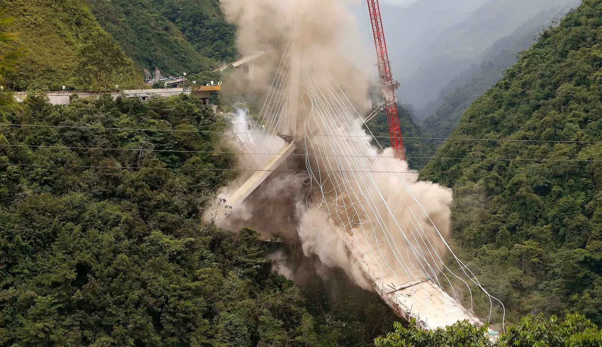 Debu mengepul ke udara saat peruntuhan sebuah jembatan gantung oleh para insinyur di Chirajara, Kolombia, Rabu (11/7). Sebelumnya, sebagian jembatan runtuh dan menewaskan sembilan pekerja saat pembangunannya pada Januari lalu. (AP Photo/Fernando Vergara)