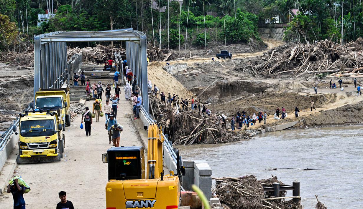 Akses utama yang menghubungkan Banda Aceh-Medan sempat lumpuh dan distribusi logistik terganggu. Tampak dalam foto, warga menyeberangi sungai di jembatan yang baru dibangun yang menghubungkan Aceh dan Provinsi Sumatera Utara setelah hancur akibat banjir bandang di Sungai Peusangan, Distrik Bireuen, Provinsi Aceh, Selasa 9 Desember 2025. (CHAIDEER MAHYUDDIN/AFP)