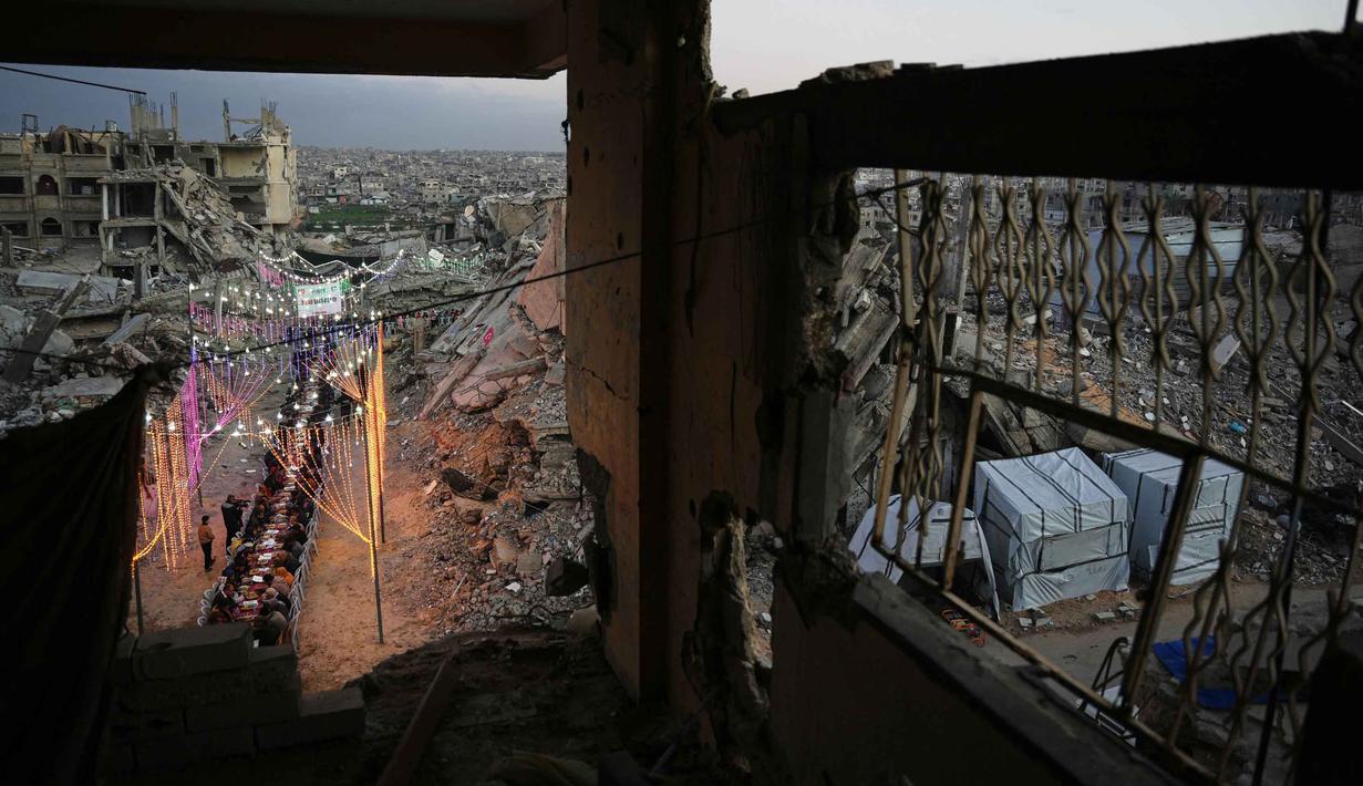 Warga Palestina di Gaza terpaksa beribadah di masjid-masjid yang rusak parah atau di antara puing-puing bangunan. Tampak dalam foto, warga Palestina duduk di meja panjang di tengah reruntuhan bangunan yang hancur untuk berbuka puasa bersama, selama bulan suci Ramadan di Khan Younis, Jalur Gaza, Kamis 19 Februari 2026. (AP Photo/Abdel Kareem Hana)