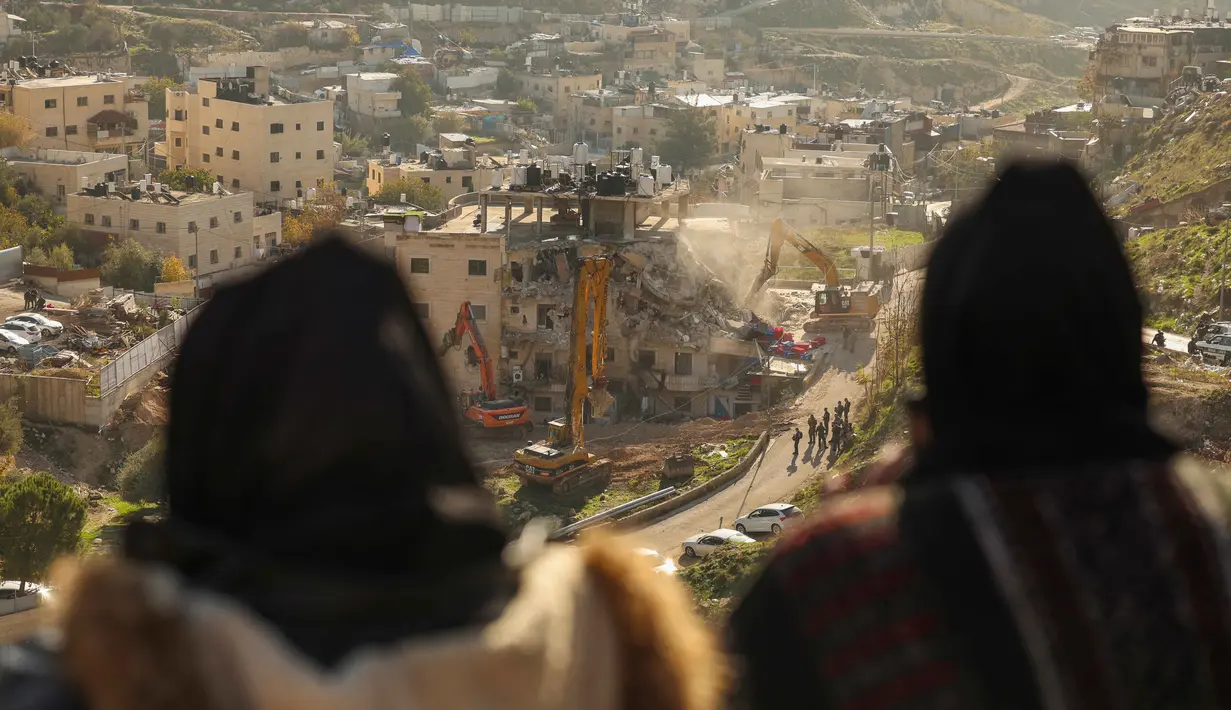 Para perempuan Palestina menyaksikan pasukan Israel yang menggunakan ekskavator merobohkan sebuah bangunan yang dibangun tanpa izin di lingkungan Wadi Qaddum, Yerusalem timur, pada Senin 22 Desember 2025. Ratusan warga Palestina terusir saat buldoser-buldoser Israel meratakan sebuah bangunan tempat tinggal empat lantai di wilayah Yerusalem Timur. (Ahmad GHARABLI/AFP)