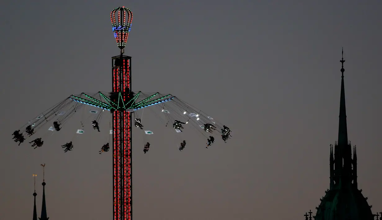 Pengunjung menaiki wahana ayunan ontang-anting di depan gereja St. Paul saat festival bir Oktoberfest di Munich, 27 September 2018. Festival yang merupakan salah satu acara paling terkenal di Jerman ini sudah ada sejak tahun 1800an. (AP/Matthias Schrader)