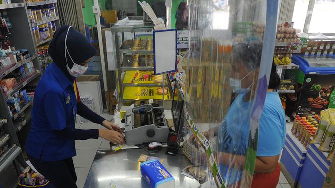 Pekerja melayani pembeli dari balik plastik pembatas pada sebuah minimarket di kawasan Cinere, Depok, Jawa Barat, Rabu (8/4/2020). Penggunaan plastik pembatas tersebut bertujuan untuk mengantisipasi penyebaran virus corona atau COVID-19 sebagai bentuk Physical Distancing. (merdeka.com/Arie Basuki)