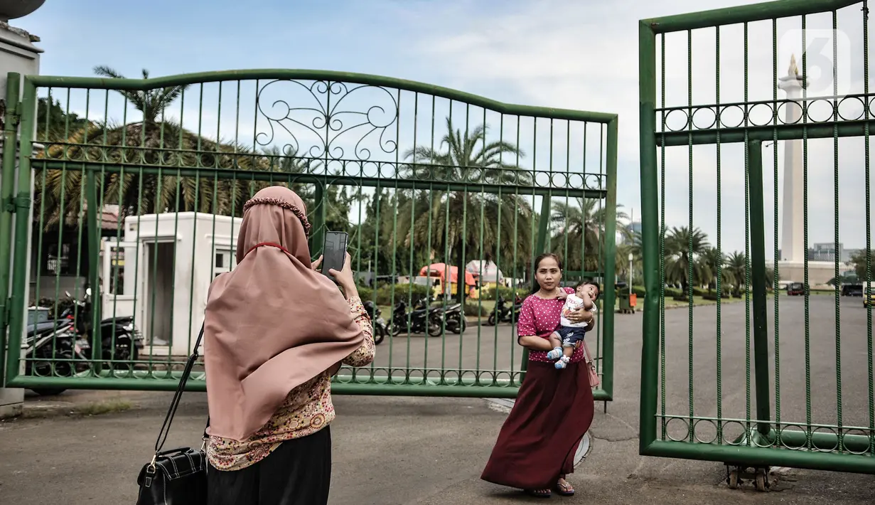 Warga berfoto di depan gerbang masuk Monumen Nasional (Monas), Jakarta, Minggu (15/11/2020). Meski masih ditutup untuk umum sejak awal pandemi Covid-19, kawasan Monas tetap ramai dikunjungi warga untuk sekadar mengisi akhir pekan. (merdeka.com/Iqbal S Nugroho)