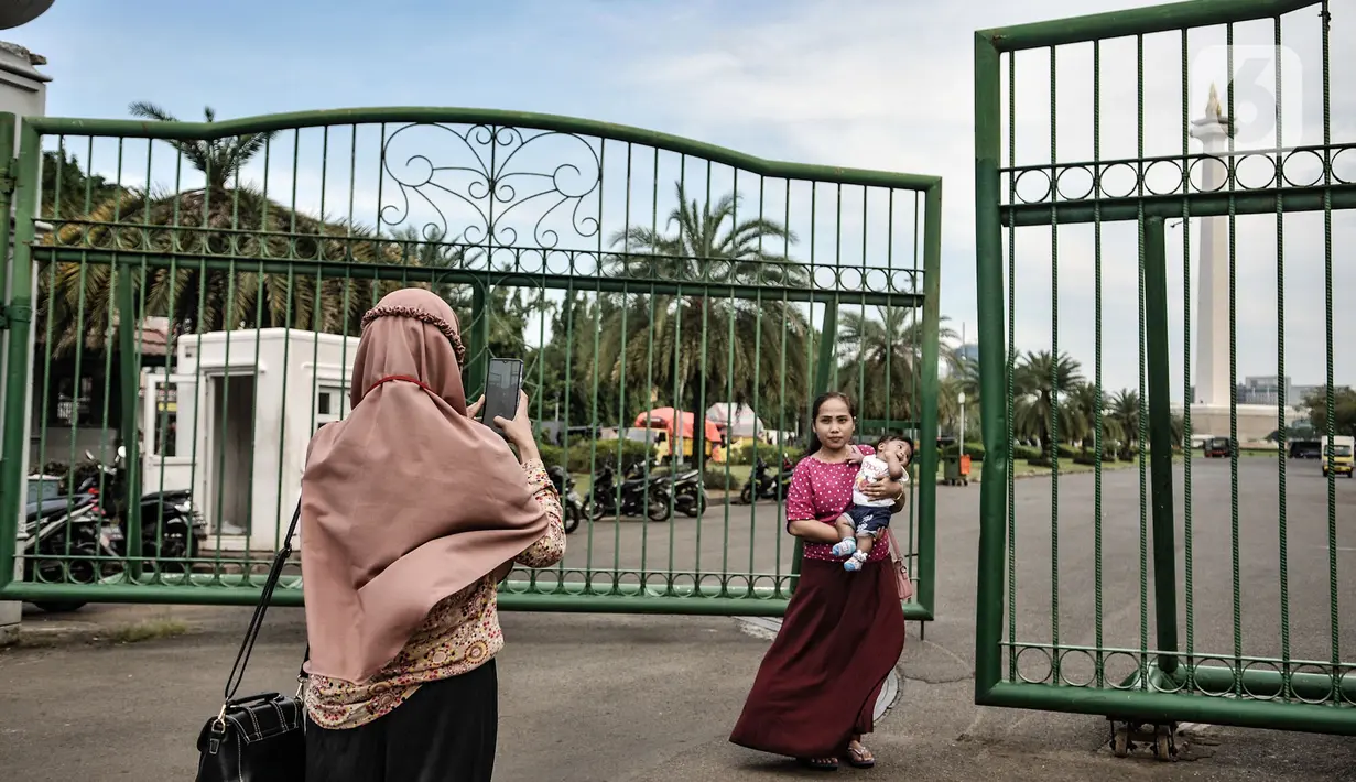 Warga berfoto di depan gerbang masuk Monumen Nasional (Monas), Jakarta, Minggu (15/11/2020). Meski masih ditutup untuk umum sejak awal pandemi Covid-19, kawasan Monas tetap ramai dikunjungi warga untuk sekadar mengisi akhir pekan. (merdeka.com/Iqbal S Nugroho)