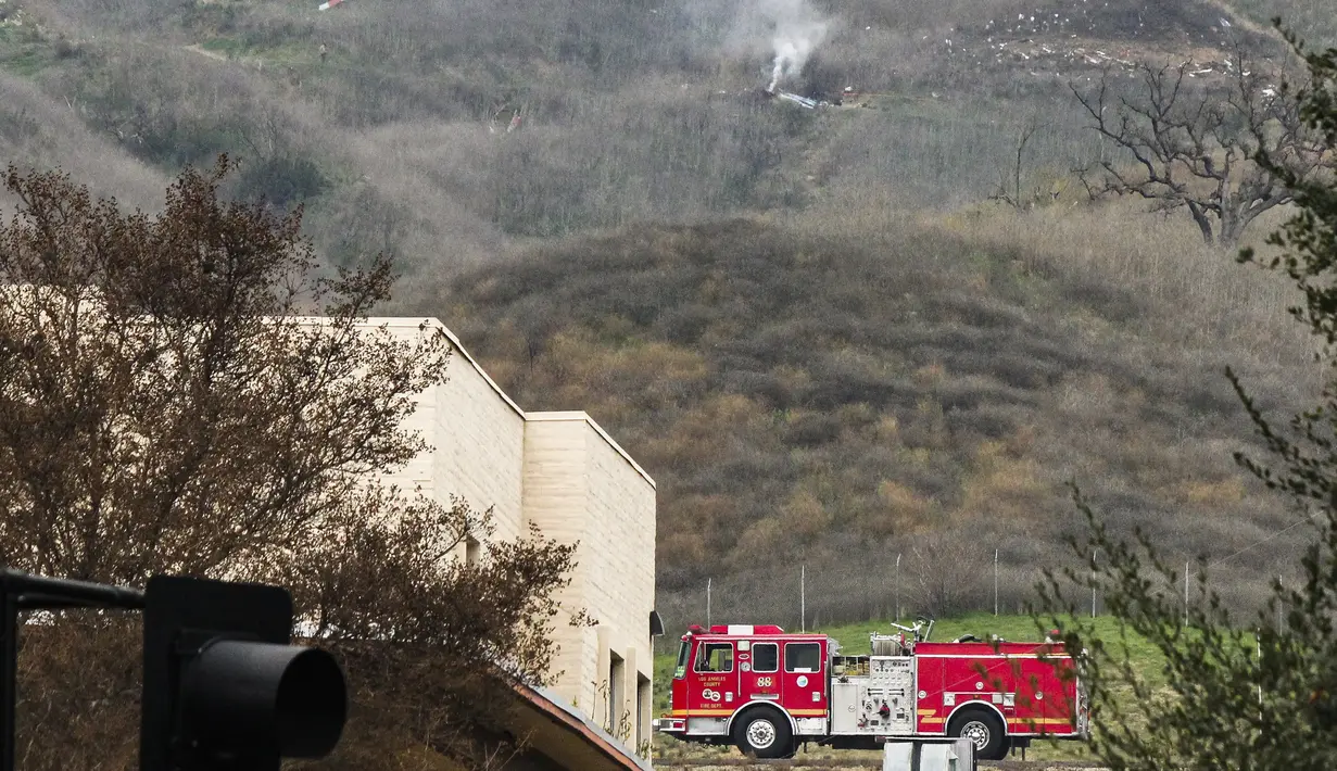 Seorang perwira sheriff (kiri) berdiri di dekat helikopter yang ditumpangi pebasket NBA Kobe Bryant di sisi bukit di Calabasas, California (26/1/2020). Sementara istri Kobe, Vanessa, diyakini tidak ikut dalam penerbangan nahas tersebut. (AP Photo/John Antczak)