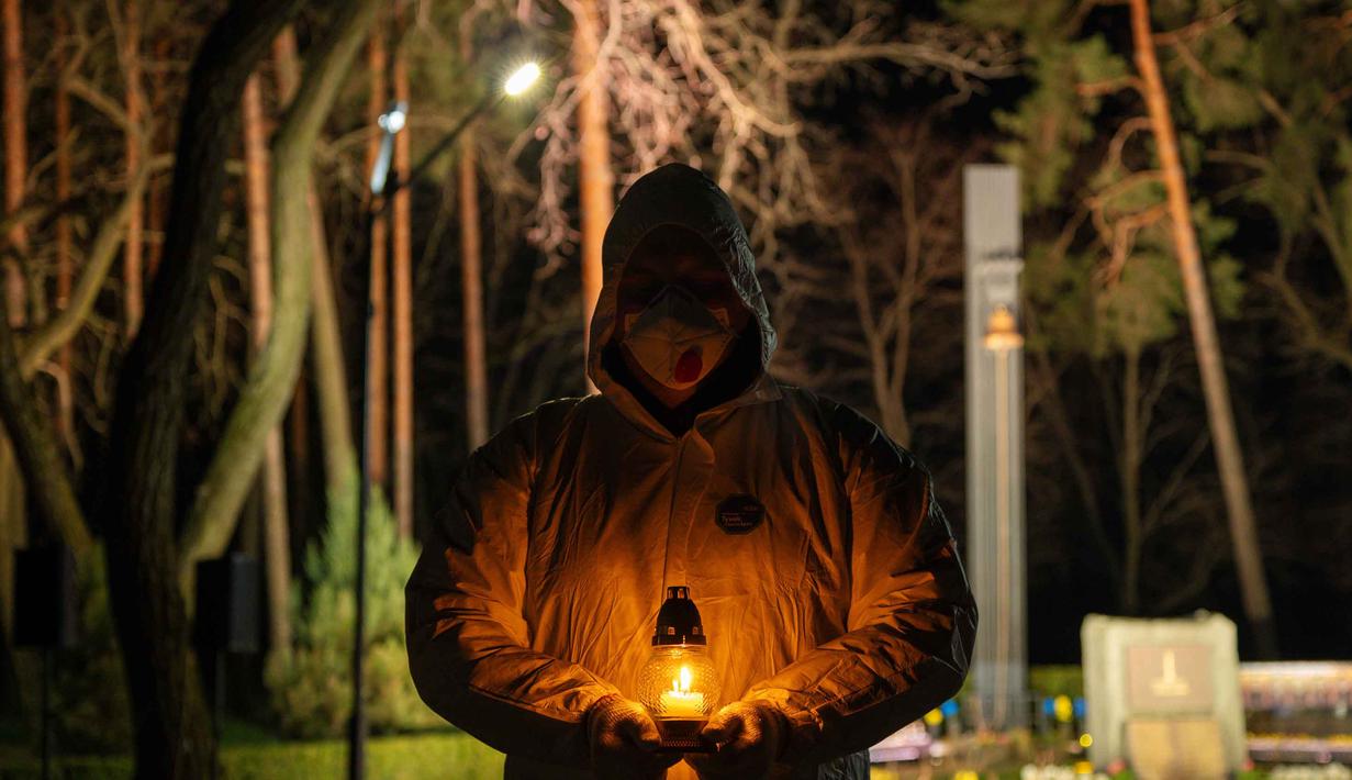 Seorang pria yang mengenakan pakaian pelindung putih memegang lilin selama upacara peringatan yang didedikasikan untuk petugas pemadam kebakaran dan pekerja yang meninggal setelah bencana nuklir Chernobyl, menjelang peringatan 40 tahunnya di Slavutych, Ukraina, Sabtu, 25 April 2026. (AP Photo/Dan Bashakov)