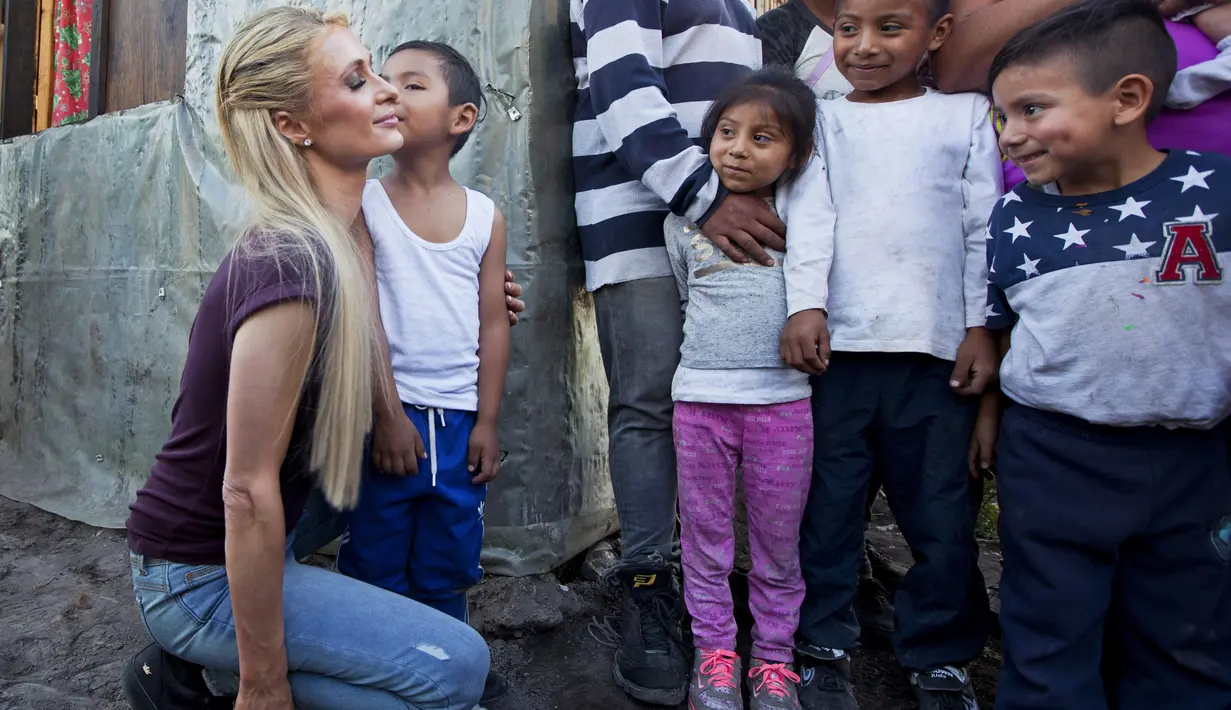 Aktris Paris Hilton dicium seorang anak saat mengunjungi keluarga yang terkena dampak gempa bumi pada September 2017 di San Gregorio Atlapulco, Meksiko (12/11). Paris Hilton tampil mengenakan kaos, jeans dan sepatu hitam. (AFP Photo/Antonio Nava)