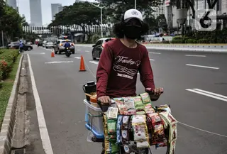 Pedagang kopi keliling saat melintas di Jalan Jenderal Soedirman, Jakarta, Minggu (11/10/2020). Gugus Tugas Percepatan Penanganan Covid-19 mencatat adanya pelambatan kenaikan kasus positif atau aktif di Ibu Kota selama sebulan pemberlakukan PSBB yang diperketat. (merdeka.com/Iqbal S. Nugroho)