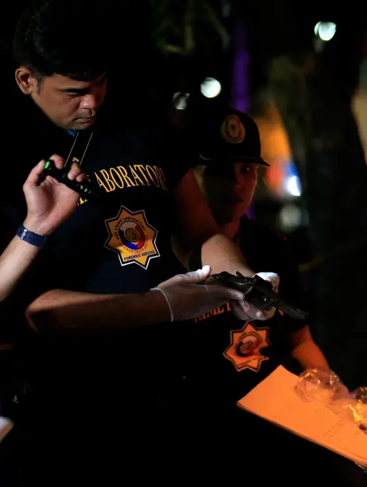 Petugas memeriksa pistol yang berada di dekat jenazah pria diduga bandar narkoba di pinggir jalan Malate, Manila (29/8). Kondisi jenazah ini sama seperti tragedi sebelumnya, yakni luka tembak dan pistol di tangan. (REUTERS/Romeo Ranoco)