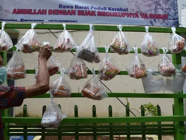 Warga mengambil sembako yang digantung di rak kayu sisi jalan di kawasan Rawa Barat, Jakarta Selatan, Kamis (14/5/2020). Selama masa pandemi COVID-19, pihak kelurahan dan masjid sekitar menyediakan paket berisi mi instan, telur, dan masker untuk warga yang membutuhan. (merdeka.com/Imam Buhori)