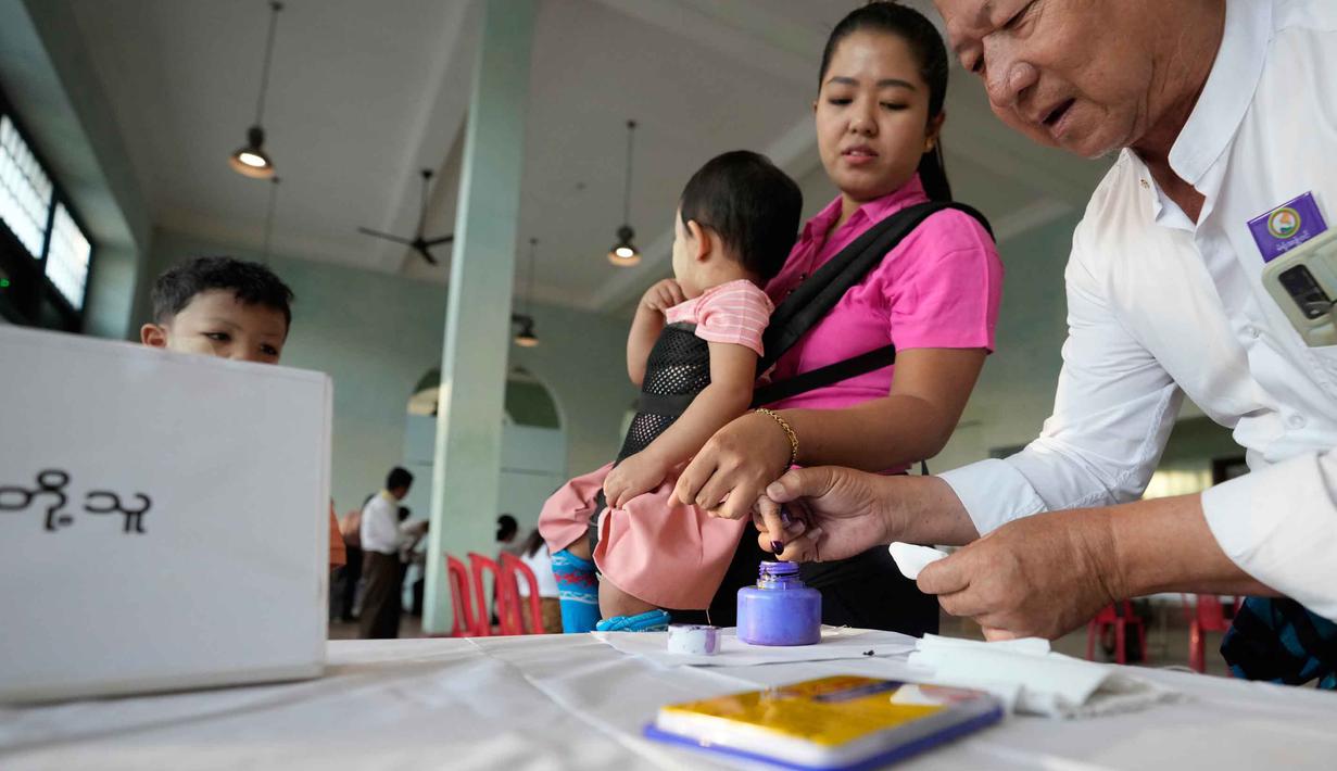Tahap pertama pemilu Myanmar digelar hari ini, Minggu 28 Desember 2025, dimulai pukul 06.00 waktu setempat di sejumlah daerah, termasuk Yangon, Mandalay, dan ibu kota Naypyidaw. Tampak dala foto, seorang pemilih, sambil menggendong anaknya, mencelupkan jarinya ke dalam botol tinta setelah memberikan suara di tempat pemungutan suara di Yangon, Myanmar, Minggu, 28 Desember 2025,  (AP Photo/Thein Zaw)