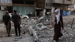Seorang wanita Palestina berjalan melewati orang-orang yang memeriksa puing-puing bangunan tempat tinggal setelah serangan Israel di Kota Gaza pada Kamis 4 Juni 2026. (Omar AL-QATTAA/AFP)
