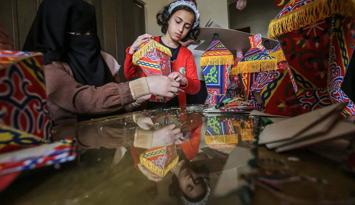 Anggota keluarga Palestina al-Yaqoubi berkumpul di sekitar meja membuat lentera bulan suci Ramadan untuk dijual selama penerapan lockdown di Khan Yunis, di Jalur Gaza, 15 April 2020. Biasanya menjelang Ramadan, warga Palestina berburu lentera tradisional untuk dijadikan dekorasi. (SAID KHATIB / AFP)