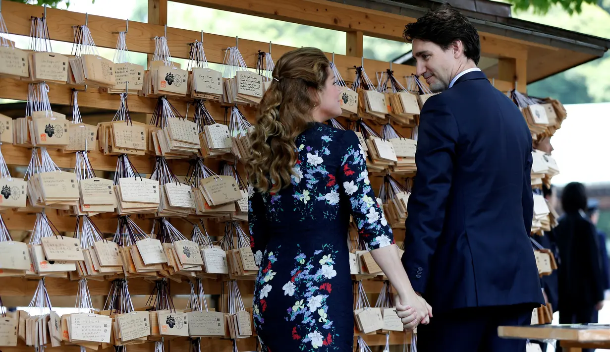  Perdana Menteri Kanada Justin Trudeau bersama istrinya Sophie Gregoire Trudeau saling pegangan tangan saat mereka mengantungkan 'Ema' atau sebuah harapan yang mereka tulis di sebuah kayu di Kuil Meiji di Tokyo, Jepang (24/5).  (REUTERS/Issei Kato)