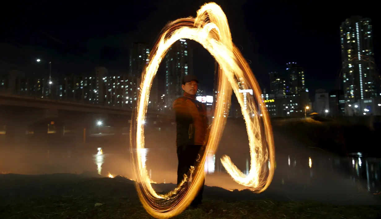 Warga memutarkan kaleng berisi kayu yang dibakar jelang perayaan "Jeongwol Daeboreum"di sebuah taman di Seoul, Korea Selatan, Minggu (21/2). Tarian api ini merupakan bagian dari perayaan Imlek ala Korea. (REUTERS/Kim Hong-Ji)