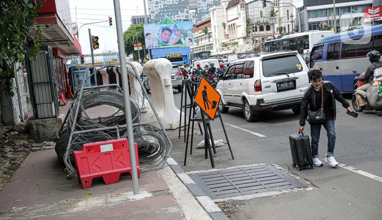 Warga berjalan kaki di samping barrier atau penghalang di kawasan Harmoni, Jakarta, Kamis (27/10/2022). Barrier yang biasa digunakan ketika terjadi demonstrasi Itu menyulitkan pejalan kaki saat melintas di trotoar. (Liputan6.com/Faizal Fanani)