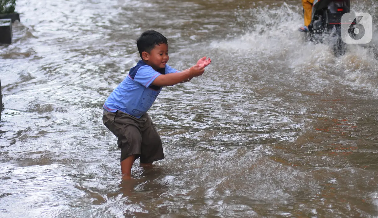 Seorang anak bemain air banjir yang merendam Jalan Benteng,  Duta Kranji, Kalibaru, Bekasi, Jawa Barat, Jumat (24/2/2023). Hujan yang turun di Bekasi sejak Kamis malam mengakibatkan sejumlah wilayah di Bekasi tergenang hingga lebih dari 50 cm. (merdeka.com/Imam Buhori)