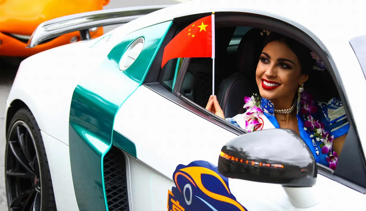 Seorang kontestan Miss World tersenyum sambil membawa bendera China saat mengikuti pawai menggunakan supercar di Sanya, Provinsi Hainan, China, (7/11). Pawai ini membuka kontes kecantikan Miss World ke-67. (AFP Photo/Str/China Out)