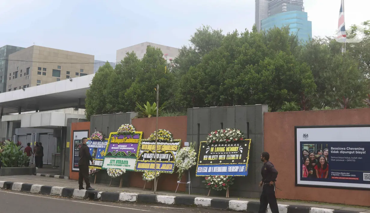 Petugas berdiri di dekat karangan bunga duka cita atas meninggalnya Ratu Elizabeth II di depan Kedutaan Besar (Kedubes) Inggris, kawasan Kuningan, Jakarta, Jumat (9/9/2022).  Ratu Elizabeth II meninggal di tengah anggota keluarga yang datang untuk berkunjung ke sana. (Liputan6.com/Herman Zakharia)