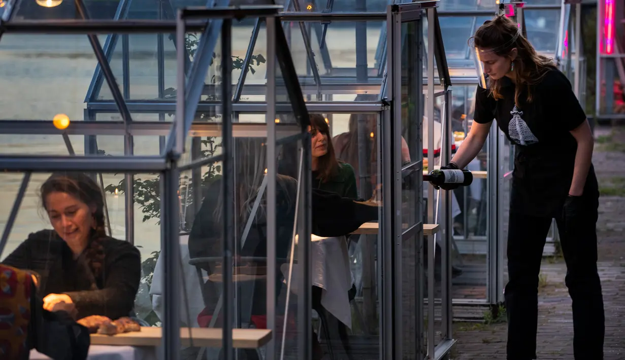 Staf menyajikan minuman kepada pelanggan dalam kabin kaca berkonsep "quarantine greenhouses" selama uji coba, ketika Belanda berjuang melawan penyebaran COVID-19, di restoran Mediamatic, Amsterdam pada 5 Mei 2020. (AP/Peter Dejong)