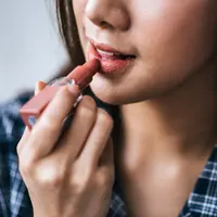 Seorang perempuan sedang mengaplikasikan lipstik di bibirnya (Foto Dok: Freepik/jcomp).